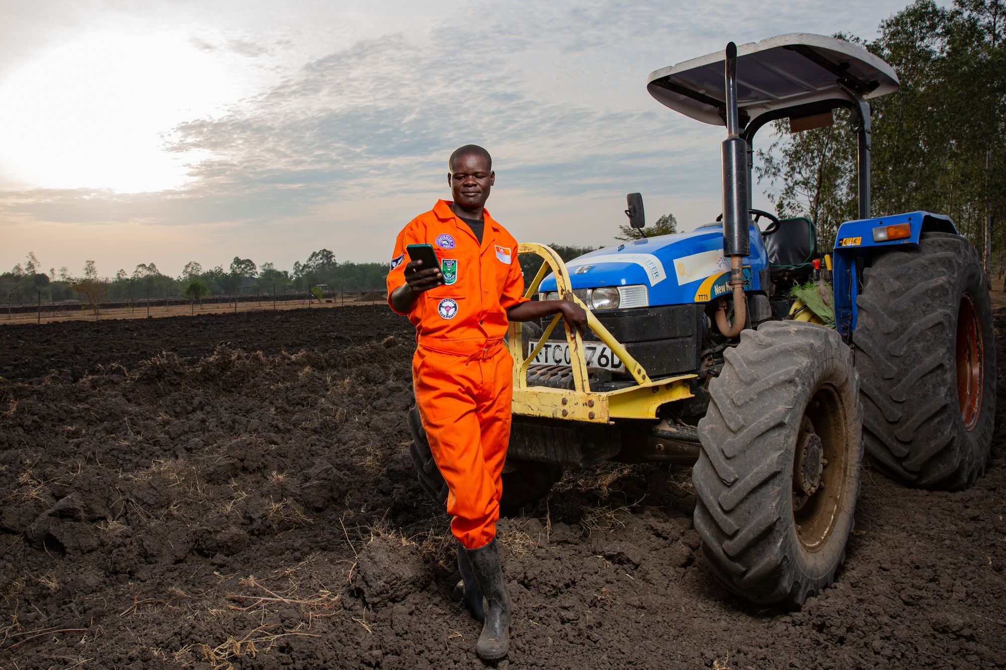 Hello Tractor operator checking the platform on his phone beside his tractor in a freshly ploughed field at sunset